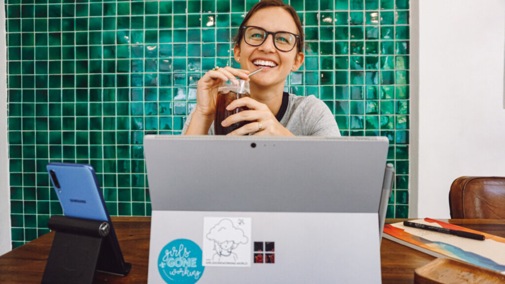 smiling woman sipping a cold drink behind her computer