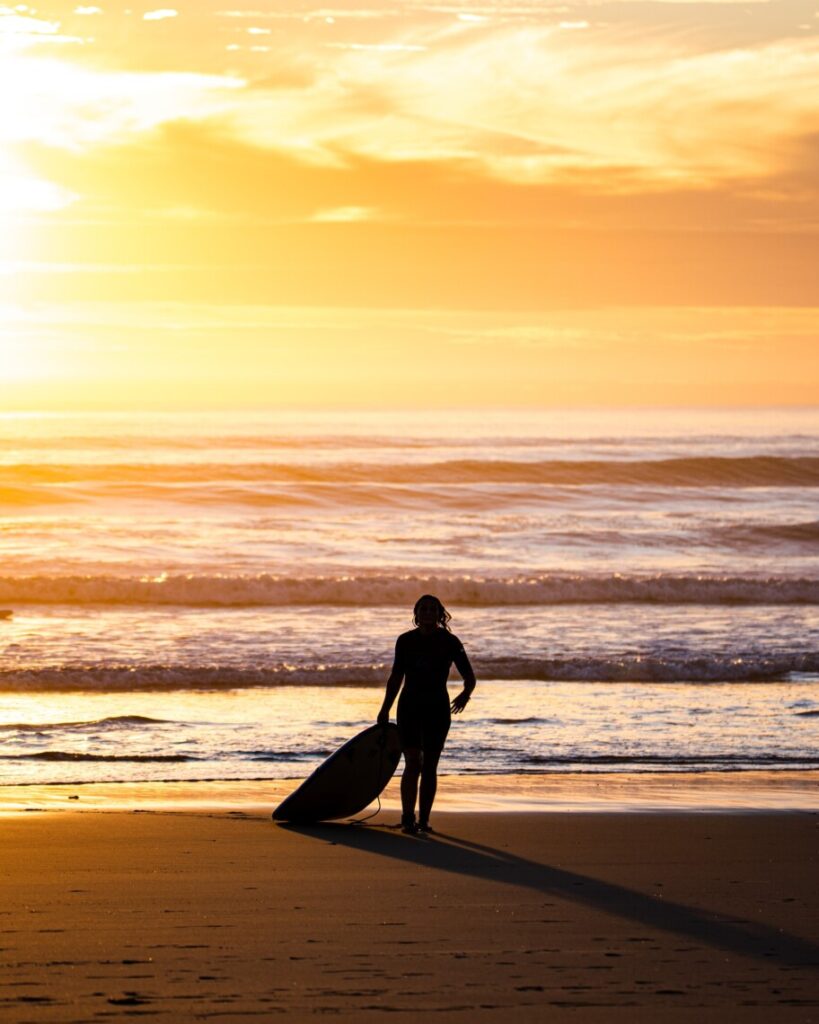 silhouet of a person with a surfboard walking on the beach at sunset