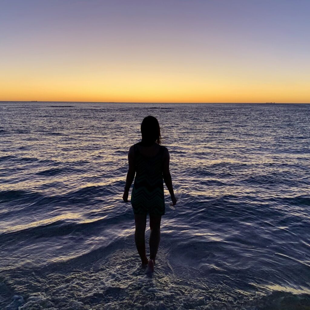 silhouet of a woman walking through the ocean at sunset