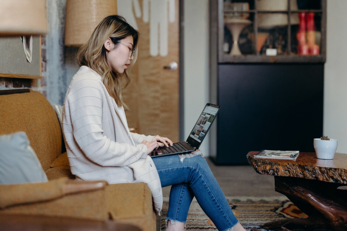 A woman sits on a couch in an apartment on her laptop