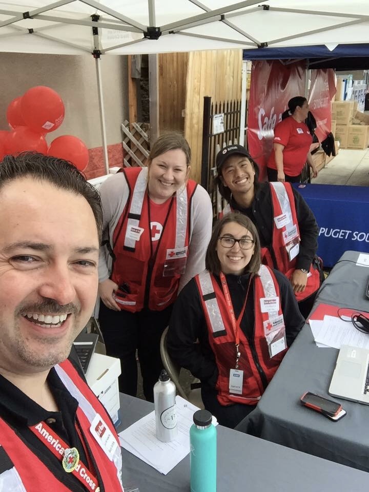Four American Red Cross volunteers smile for the camera, wearing American Red Cross vests and lanyards