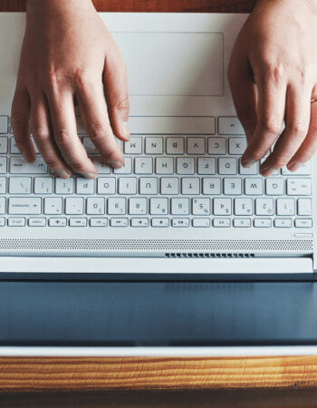 Hands typing on a keyboard with the Pinterest icon on the screen